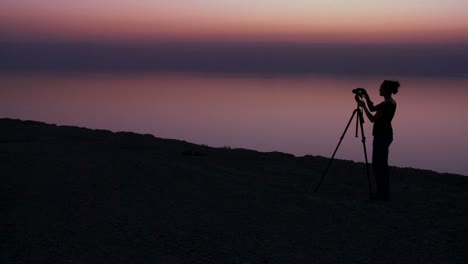 A-woman-photographer-takes-pictures-in-a-purple-golden-glow-after-sunset-behind-the-Dead-Sea-in-Jordan