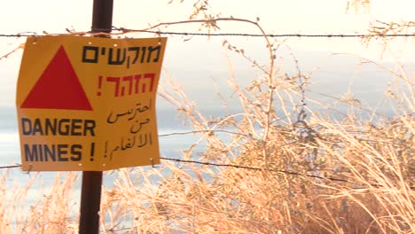 Pan-across-to-a-sign-warning-in-English-Arabic-and-Hebrew-that-mines-are-nearby-along-the-Israel-border-with-Syria