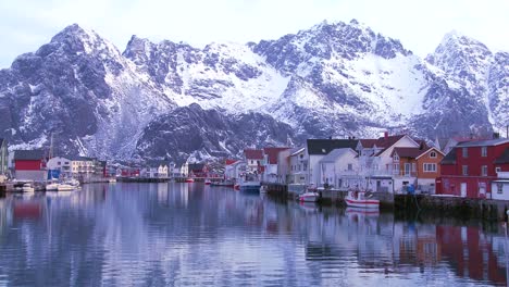 Snow-covered-mountains-are-reflected-in-a-harbor-in-a-small-fishing-village-in-the-Arctic-Lofoten-Islands-Norway-1
