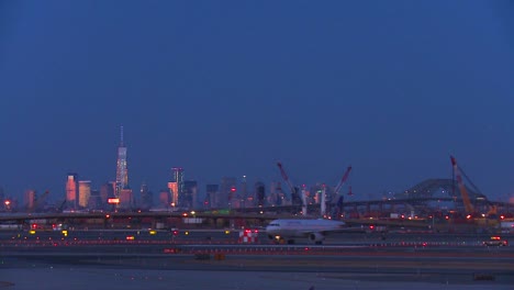 Flugzeuge-Taxi-Am-Flughafen-Newark-In-Der-Abenddämmerung-Mit-Der-Skyline-Von-Manhattan,-Die-Im-Hintergrund-Leuchtet