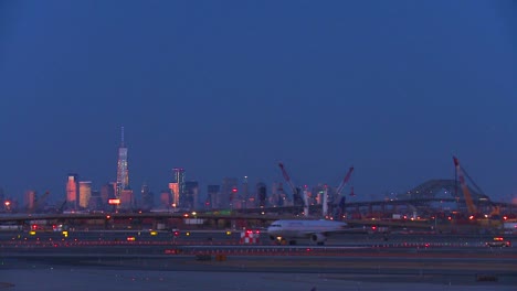 Aviones-Taxi-En-El-Aeropuerto-De-Newark-Al-Anochecer-Con-El-Horizonte-De-Manhattan-Brillando-En-El-Fondo