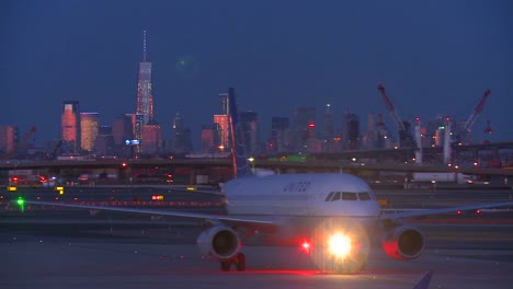 Flugzeuge-Taxi-Am-Flughafen-Newark-In-Der-Abenddämmerung-Mit-Der-Skyline-Von-Manhattan,-Die-Im-Hintergrund-Leuchtet-1
