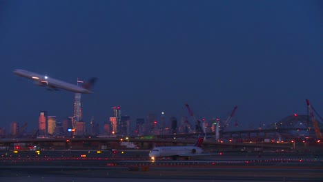Flugzeuge-Taxi-Und-Starten-Am-Flughafen-Newark-In-Der-Abenddämmerung-Mit-Der-Skyline-Von-Manhattan-Im-Hintergrund-Leuchten