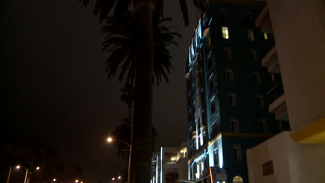 Inclinarse-Desde-Una-Calle-Concurrida-Hasta-Un-Hotel-Art-Deco-O-Un-Edificio-De-Oficinas-Por-La-Noche