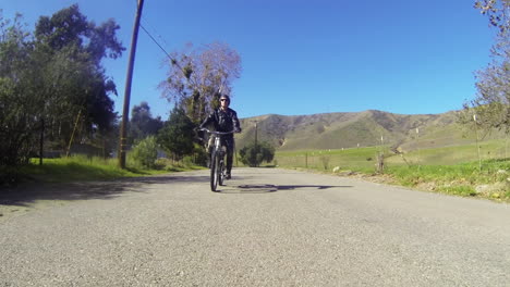 Un-Hombre-Monta-Una-Bicicleta-Motorizada-Por-El-Campo-En-Una-Carretera-De-Dos-Carriles