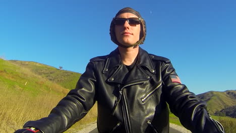 Close-up-of-a-leather-clad-mans-face-as-he-rides-a-motorized-bicycle-through-the-countryside-on-a-two-lane-road