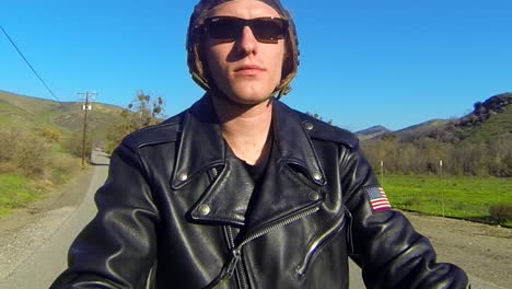 Close-up-of-a-leather-clad-mans-face-as-he-rides-a-motorized-bicycle-through-the-countryside-on-a-two-lane-road-1