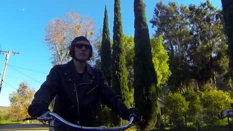 Close-up-of-a-leather-clad-mans-face-as-he-rides-a-motorized-bicycle-through-the-countryside-on-a-two-lane-road-2