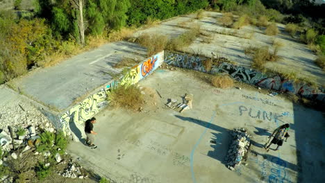 Luftaufnahme-Von-Jungen-Im-Teenageralter,-Die-Im-Mit-Graffiti-Bedeckten-Fundament-Eines-Verlassenen-Gebäudes-Skateboard-Fahren-2