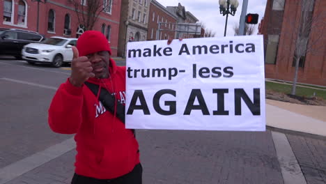 Ein-Mann-Hält-An-Einer-Amerikanischen-Straßenecke-Ein-Anti-Trump-Rallye-Schild-Hoch,-Auf-Dem-Steht,-Dass-Amerika-Wieder-Weniger-Trumpft