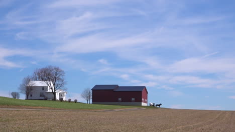 Eine-Sehr-Breite-Aufnahme-Einer-Isolierten-Amish--Oder-Mennonitenfarm-Im-Mittleren-Westen-Von-Amerika-Mit-Vorbeifahrender-Pferdekutsche