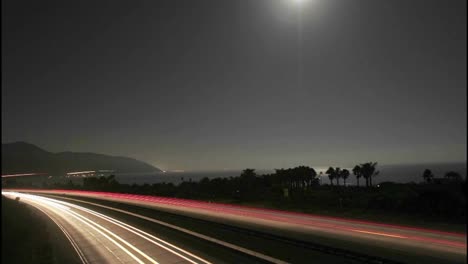 Time-lapse-of-the-moon-and-traffic-near-the-beach-at-night--