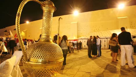 A-time-lapse-of-people-walking-pass-a-gold-colored-liquid-container-at-night-in-Morocco