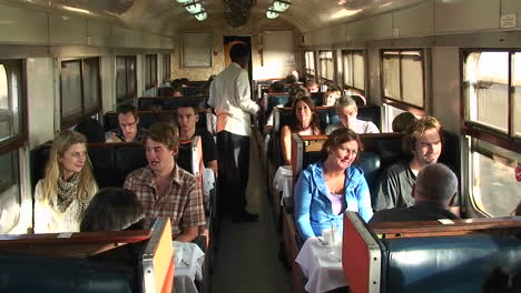 An-attendant-passes-through-a-train-car-carrying-a-plate-as-passengers-talk-and-look-out-the-window