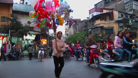 Una-Mujer-Camina-Con-Globos-Por-Una-Calle-Muy-Transitada-En-Hanoi,-Vietnam