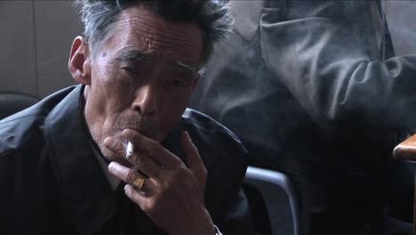 An-old-Chinese-man-smokes-a-cigarette-and-peers-at-the-camera