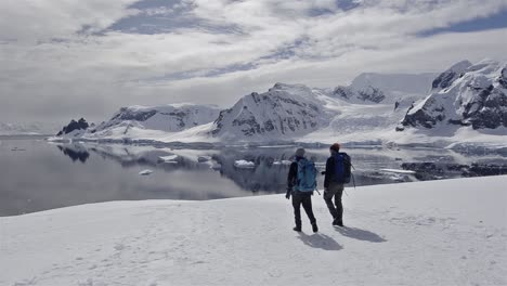 Schwenkbewegung-Von-Zwei-Wanderern-Zu-Einer-Eselspinguinkolonie-Im-Schnee-Auf-Der-Danco-Insel-In-Der-Antarktis