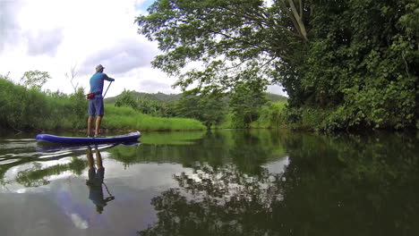 A-man-rows-a-paddleboard-down-a-river-in-Kauai-Hawaii