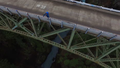 An-aerial-over-a-man-standing-on-a-steel-suspension-bridge-over-the-Skokomish-River-in-Washington-USA