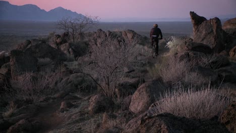 Cyclists-travel-rough-trails-in-a-desert-area-near-dusk-with-head-lights