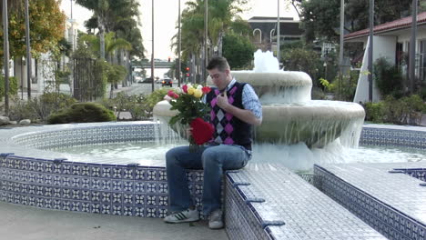 A-man-waits-excitedly-at-a-fountain-with-flowers-and-a-heartshaped-box