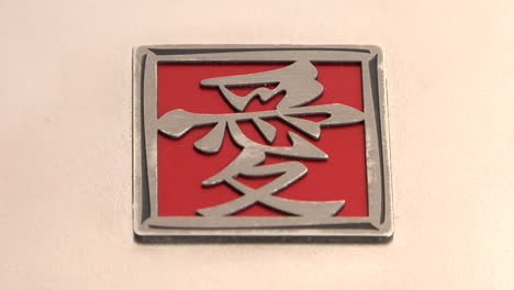 Ein-Rot-silbernes-Quadrat-Mit-Asiatischen-Schriftzeichen-Liegt-Auf-Einer-Rosa-Fläche