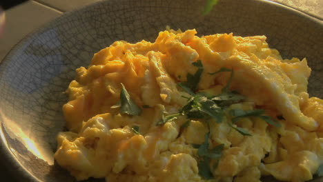 A-slow-pull-into-a-bowl-of-scrambled-eggs-as-parsley-is-chopped