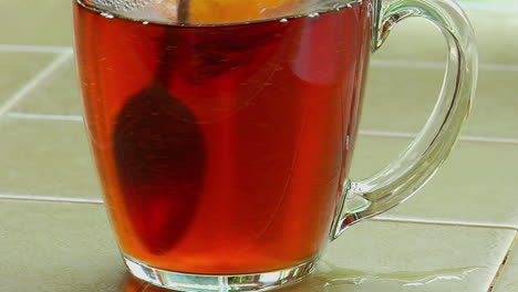 Sugar-poured-into-a-clear-glass-cup-of-tea-and-stirred-with-a-spoon