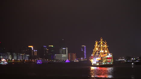 The-night-skyline-of-Shanghai-China-with-river-traffic-foreground-and-illuminated-tall-ship-passing
