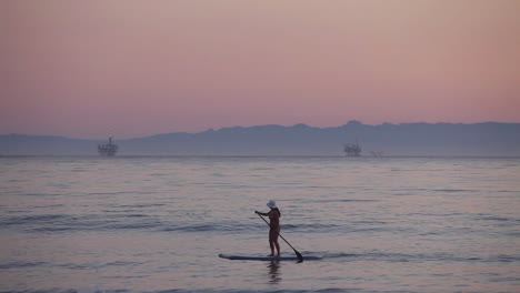 A-paddle-boarder-rows-across-the-ocean-at-sunset