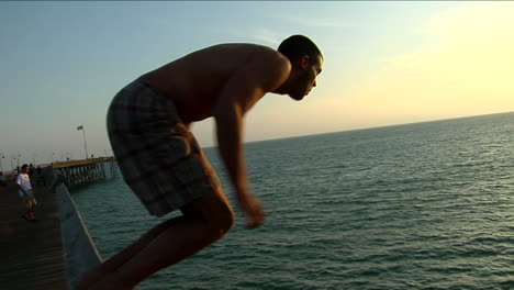 A-young-man-climbs-onto-the-rail-of-a-pier-and-plunges-into-the-sea