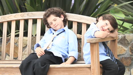 A-pair-of-boys-in-formal-dress-sit-on-a-wooden-bench--1