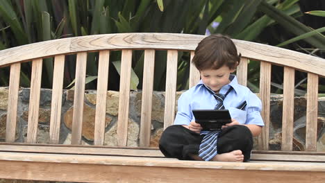 A-boy-in-formal-dress-plays-with-an-electronic-device-on-a-wooden-bench-