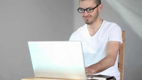 A-young-man-sits-and-smiles-as-he-starts-using-his-laptop-computer
