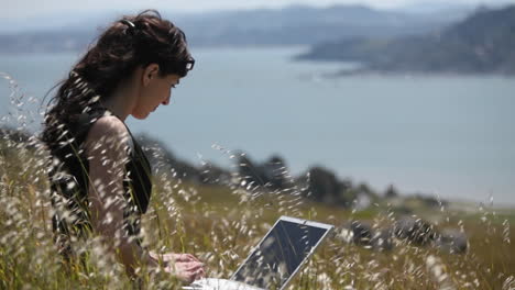 A-woman-sits-in-the-grass-and-uses-her-laptop