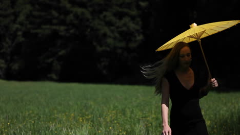 A-young-woman-walks-through-a-grassy-field-carrying-a-yellow-parasol