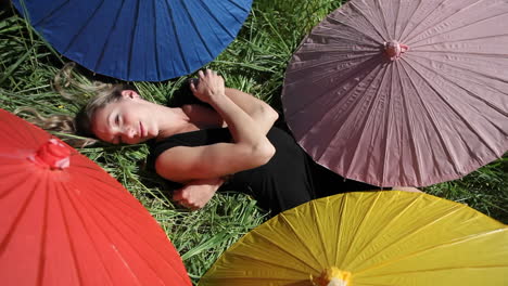 Eine-Frau-Liegt-Auf-Dem-Rücken-Auf-Einer-Wiese,-Umgeben-Von-Meinen-Verschiedenfarbigen-Regenschirmen