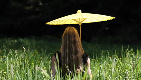 Eine-Frau-Sitzt-Mit-Einem-Gelben-Regenschirm-Im-Gras