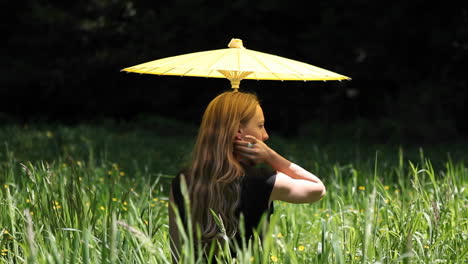 Eine-Frau-Mit-Regenschirm-Sitzt-Auf-Einem-Feld