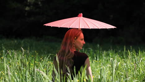 Eine-Frau-Mit-Regenschirm-Sitzt-Auf-Einem-Feld