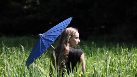 A-woman-sits-in-a-grassy-field-holding-a-blue-umbrella