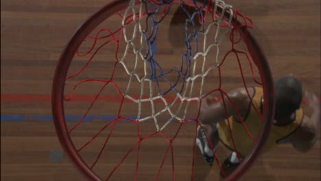A-man-throws-a-ball-into-the-hoop-hangs-on-to-the-rim-then-drops-to-the-floor