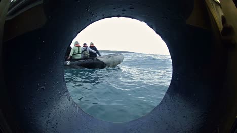 View-through-a-ship's-porthole-of-guests-departing-on-an-inflatable-raft-in-the-Galapagos-Islands-