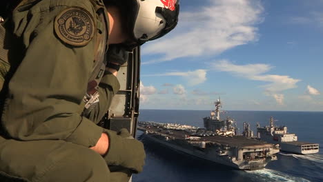 Aerial-From-A-Helicopter-With-Military-Personnel-Visible-Over-An-Aircraft-Carrier-As-Sea