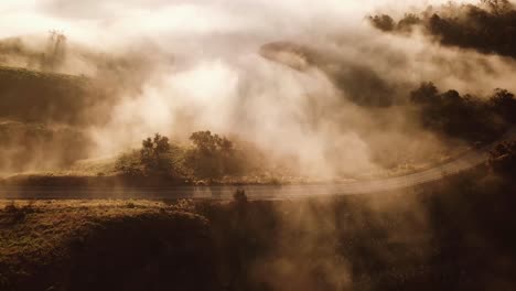 Gorgeous-Aerial-Of-A-Car-Traveling-On-A-Foggy-Road-Through-The-Countryside-At-Dawn-Or-Sunset