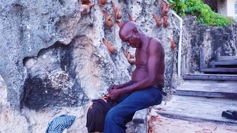 An-Old-Craftsman-Carves-Wood-Besie-A-Wall-In-Barbados-Caribbean