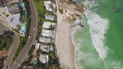 Eine-Vogelperspektive-Zeigt-Autos,-Die-Am-Strand-Von-Camps-Bay-In-Kapstadt-Südafrika-Vorbeifahren