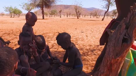 Ein-Junger-Afrikanischer-Himba-Stammesjunge-Lehnt-Sich-In-Einem-Kleinen-Dorf-In-Namibia-An-Einen-Baum