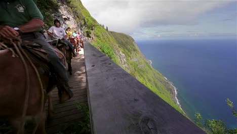 People-ride-horses-along-a-narrow-trail-in-Hawaii
