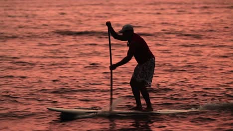 A-man-paddle-surfs-across-a-lagoon-at-sunet